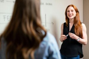 Woman infront of a white board talking to a younger woman